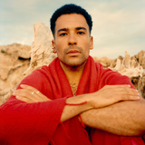 Man wearing a red fouta with arms crossed in front of desert rock formations