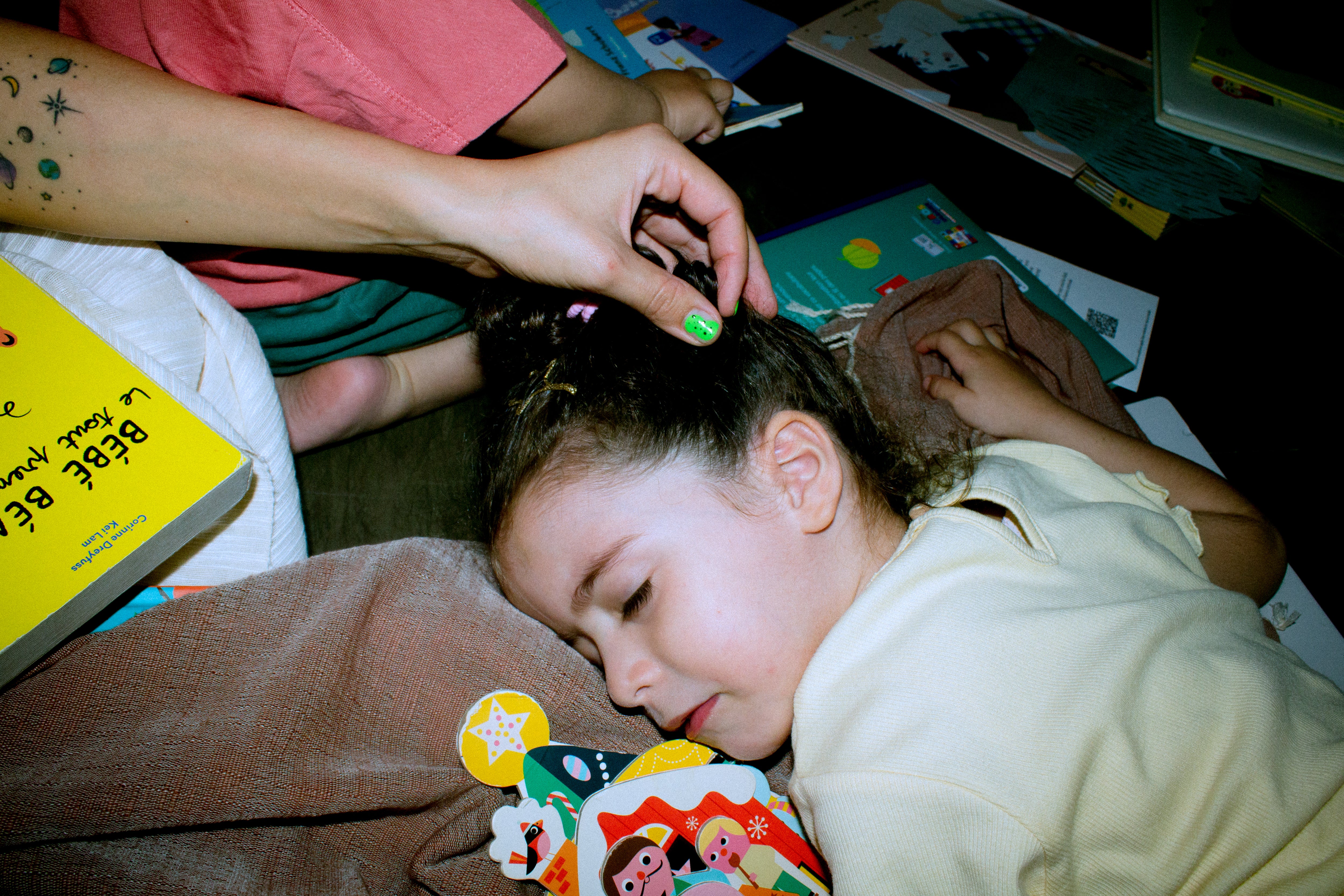 Child lying down on a fouta with a toy, being helped by an adult with hair accessories.