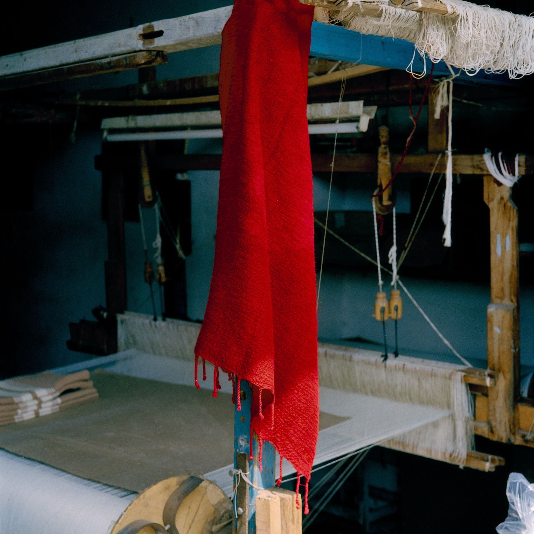 Red fabric hanging on a loom with a blue wall in the background